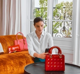 Naine pildistamas telefoniga musta laua peal olevat punast käekotti. Taustal oranz diivan, millel punane ja roosa käekott.