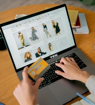 Käed sülearvuti klaviatuuril, üks hoidmas pangakaarti. Arvutiekraanil on riiete e-pood