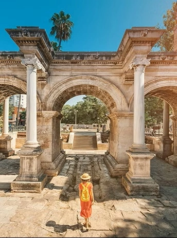 Naine oranžis kleidis ja õlgkübaraga jalutab läbi ajaloolise Hadrianuse värava Antalyas, Türgis.